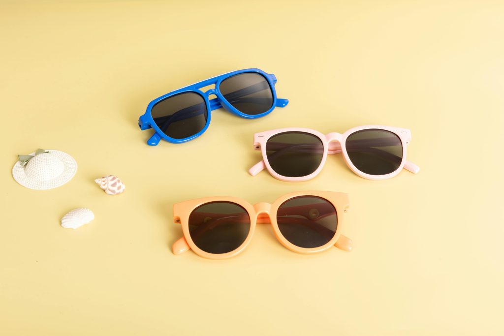 A flat lay of three colorful sunglasses on a yellow background with beach accessories. Ideal for summer and fashion themes.
